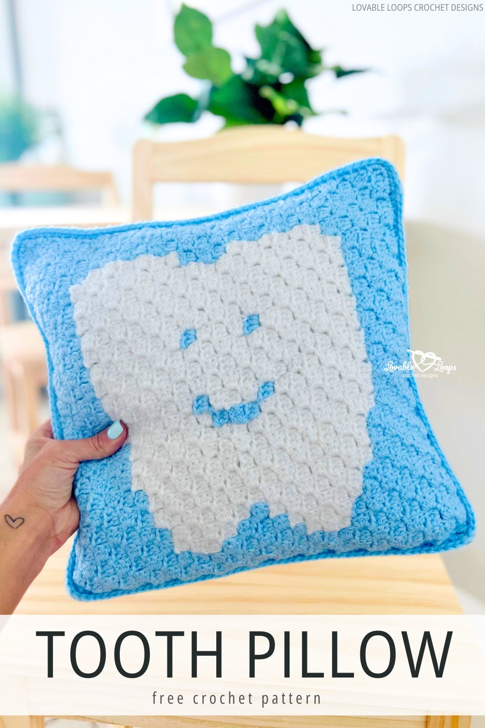 A person holding a crocheted pillow with a tooth on it