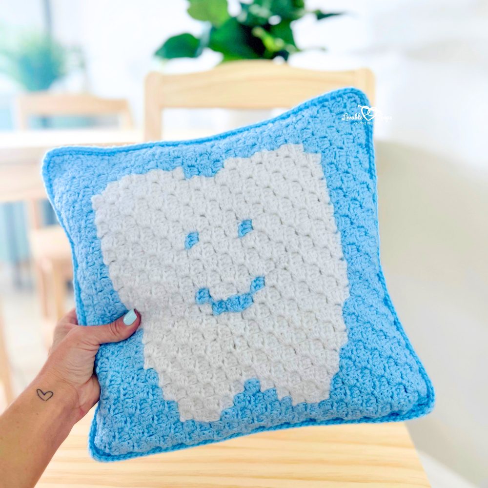 A person holding a crocheted pillow with a tooth on it