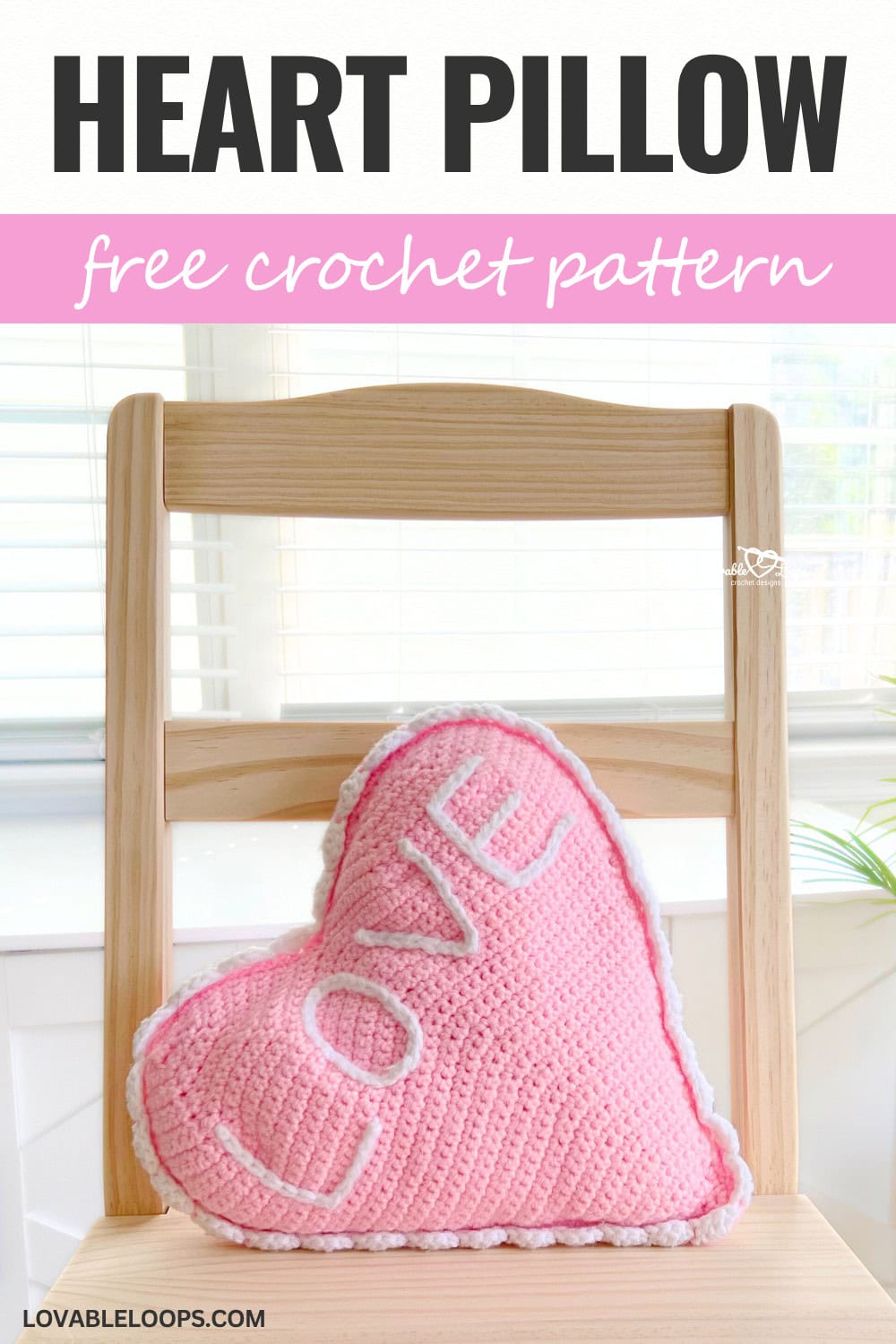 Vertical image showing a pink crochet heart pillow with “LOVE” stitched on front, sitting on a wooden chair. Text above reads “Heart Pillow” and “free crochet pattern” on a pink banner.