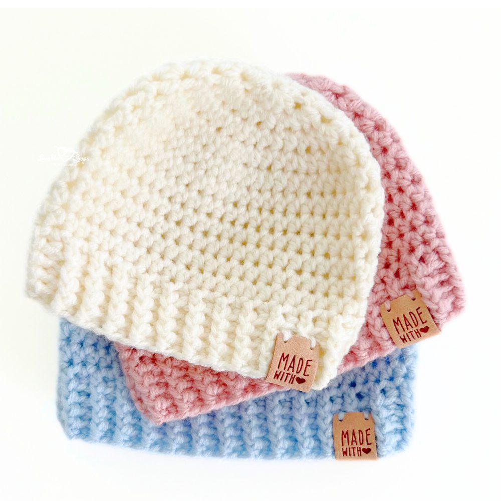 Close-up of three stacked crochet baby hats in ivory, blush pink, and baby blue. These soft handmade hats have a ribbed brim and are made using a simple and easy crochet pattern for babies.
