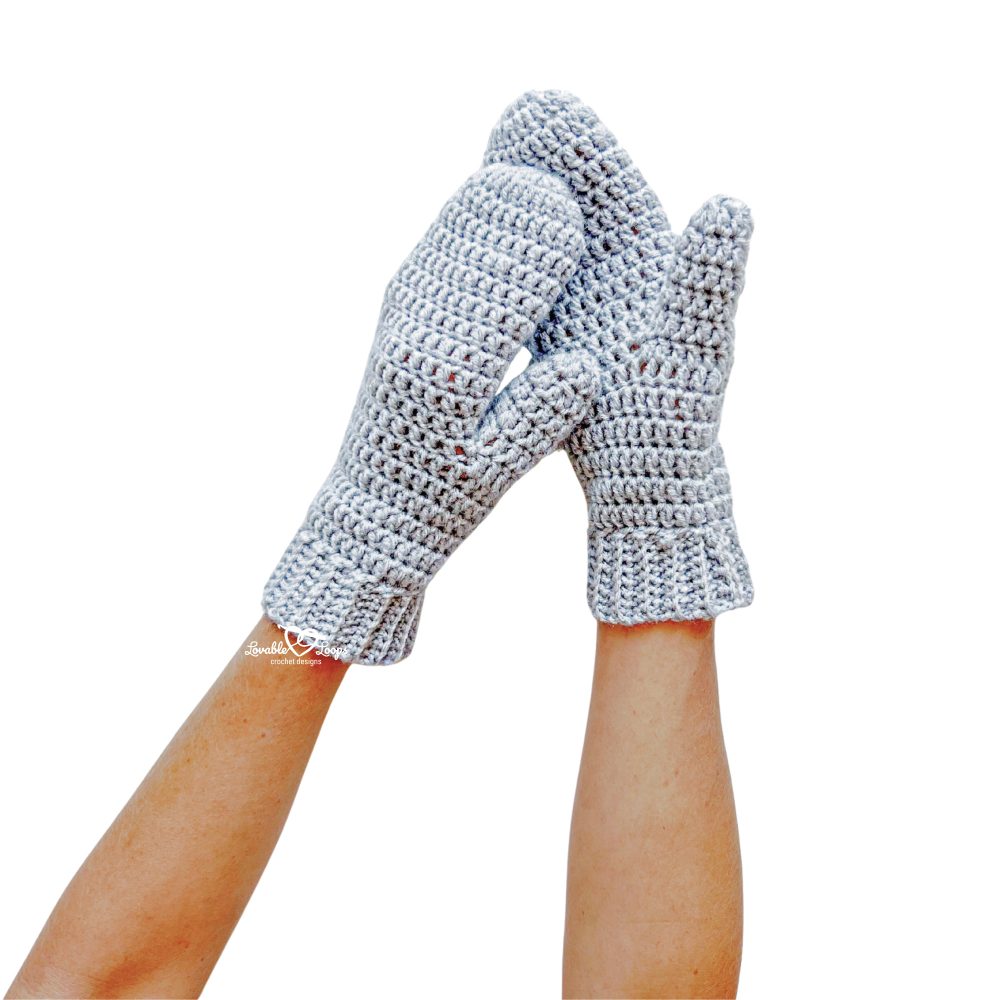 Pair of gray crochet mittens held up together in the air. The mittens feature double crochet stitches and a textured back loop only ribbed cuff. Perfect example of an easy crochet mittens pattern.