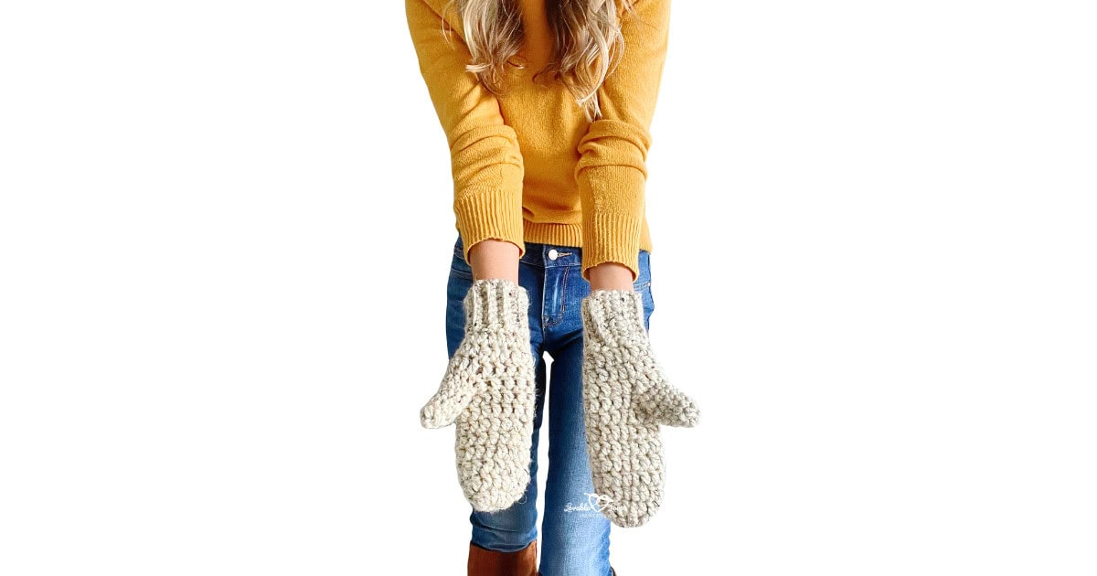 Woman wearing handmade crochet mittens made with chunky yarn in oatmeal color. Arms extended forward. Great visual for a beginner-friendly crochet mittens pattern.