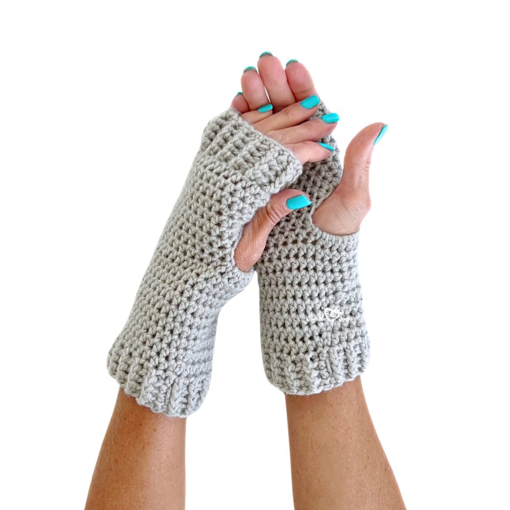 Pair of gray crochet fingerless gloves shown from a top view, worn on crossed hands. Features ribbed cuffs and thumb openings. This image highlights the cozy fit and textured design of a simple “crochet fingerless gloves pattern” made with half double crochet stitches.
