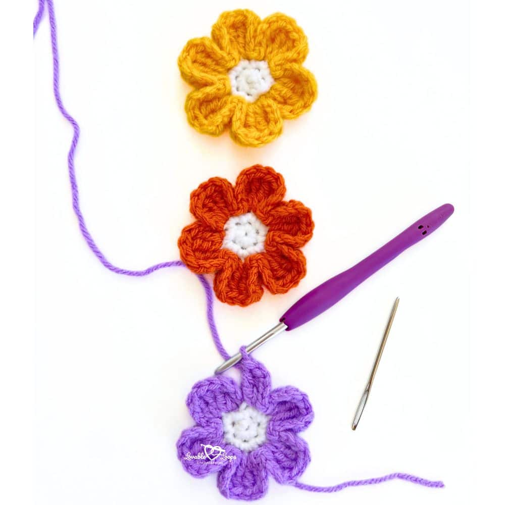 Three crochet flowers in yellow, orange, and purple yarn with a hook and yarn needle. Beginner-friendly fall crochet flower appliqué pattern.