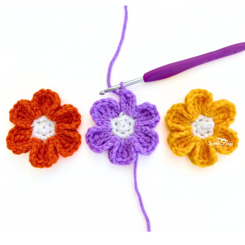 Crochet small flowers in orange, purple, and yellow with a hook attached. Free fall crochet flower pattern for beginners and quick projects.