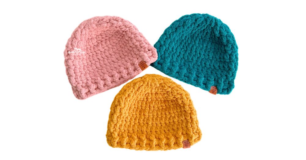 Three handmade chunky crochet beanies in pink, teal, and mustard yellow, made with soft super bulky yarn and a textured stitch pattern, perfect for a cozy winter hat.