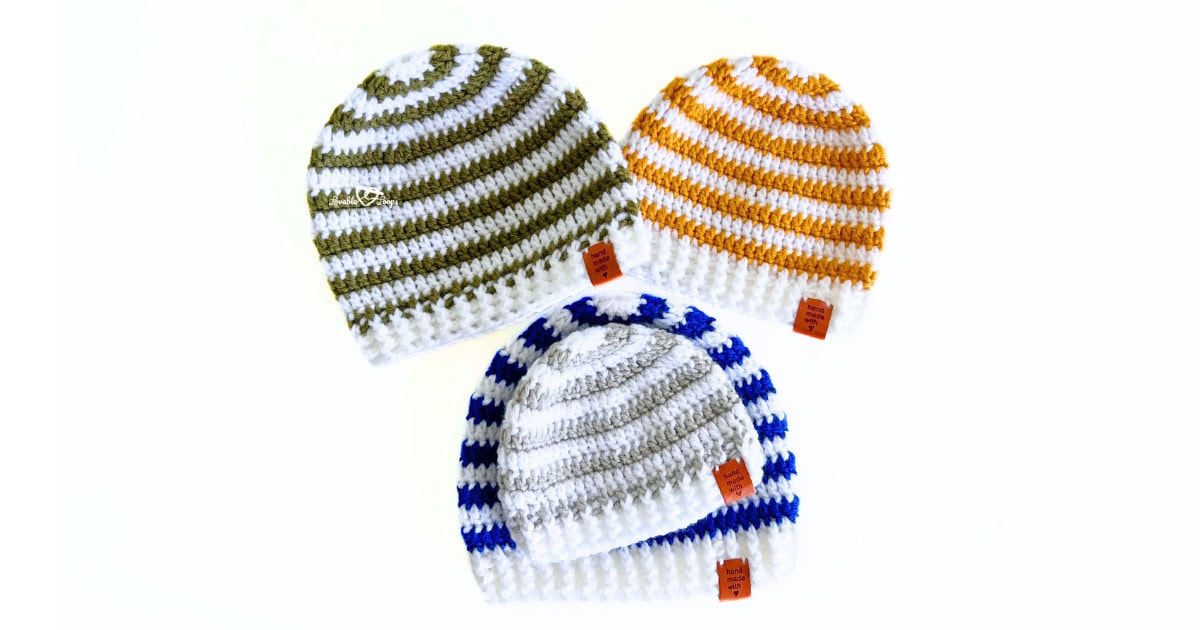 Four striped crochet beanie hats in olive green, mustard yellow, royal blue, and gray, arranged in a playful layout, each with a ribbed brim and “handmade with love” tag, made using a free beginner-friendly beanie pattern for all sizes.