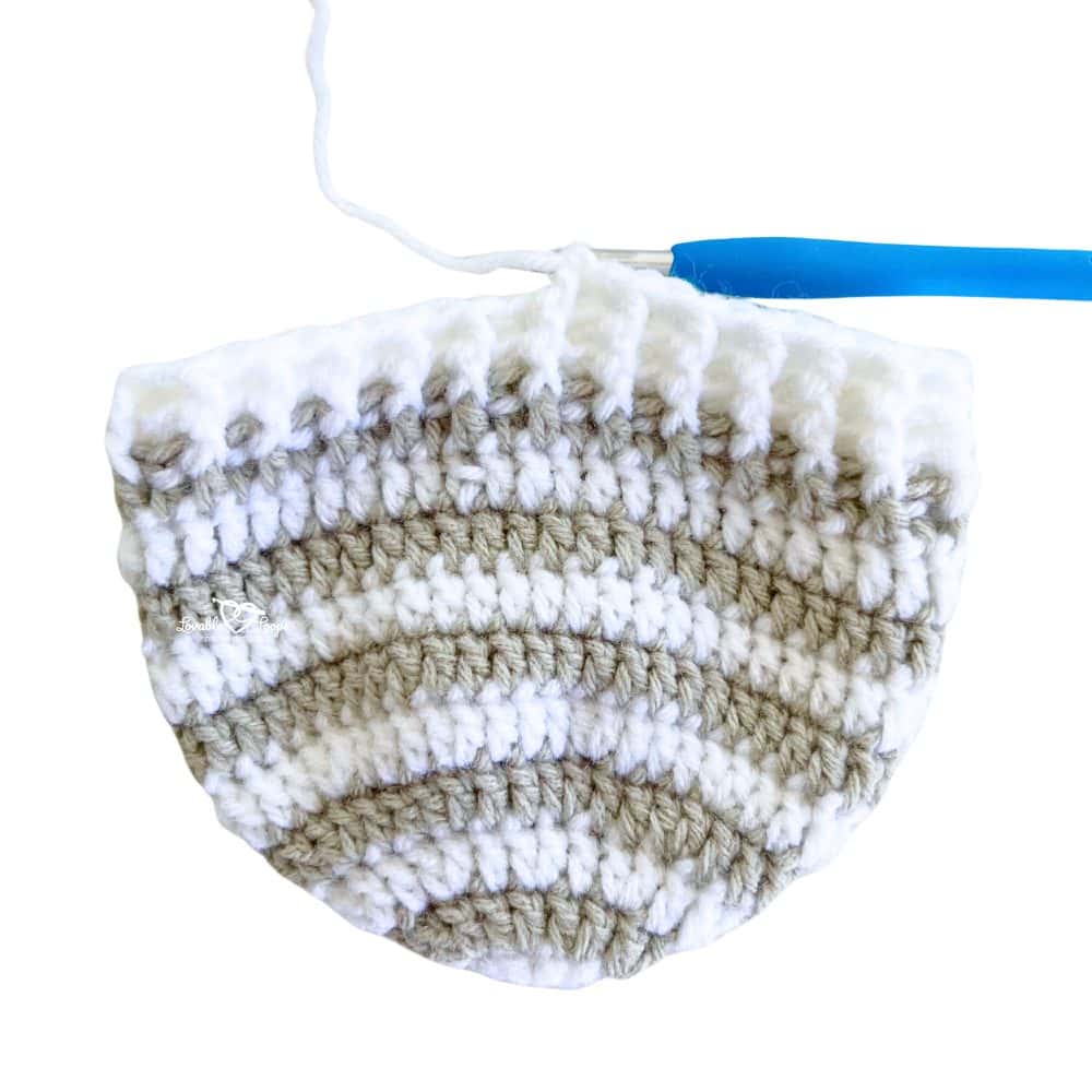 Close-up of a crochet beanie hat in progress, featuring gray and white stripes with a ribbed brim, made using a beginner-friendly crochet beanie pattern for all sizes.