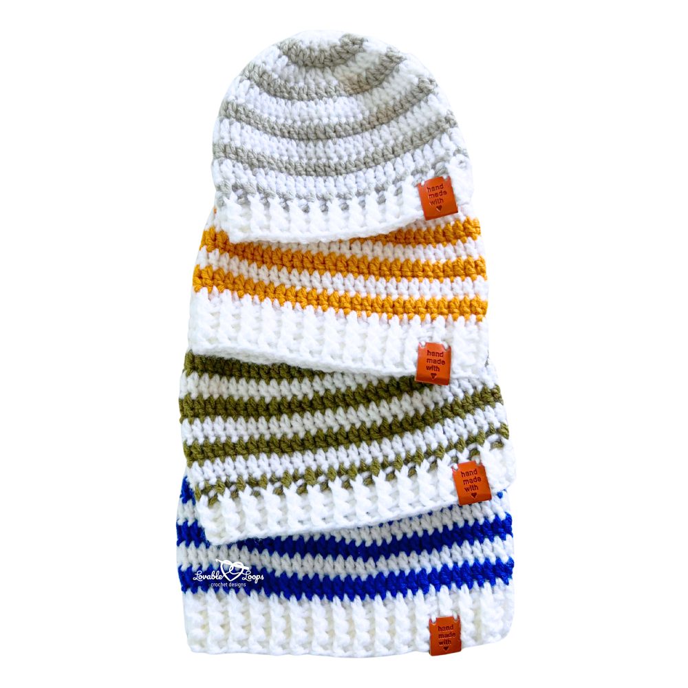 A stack of striped crochet beanie hats in neutral, mustard yellow, olive green, and blue, made using a free beginner-friendly crochet beanie pattern available in all sizes.