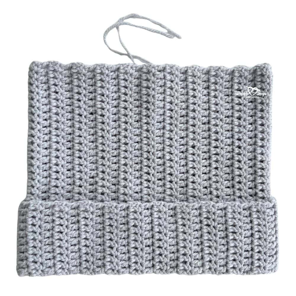 Gray crochet rectangle folded into a tube with the brim turned up, showing the step before creating the cat ears in this crochet cat hat pattern.