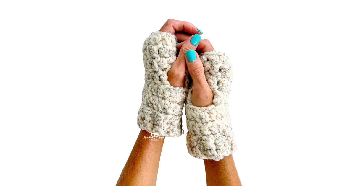 Side angle view of light gray crochet hand warmers on a model’s hands. These cozy and easy crochet hand warmers are part of a free pattern designed with simple stitches.