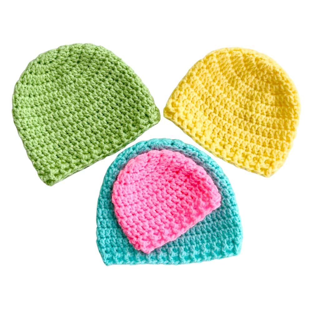 Three crochet newborn hats in green, yellow, and turquoise with a smaller pink hat stacked on top. Beginner-friendly crochet newborn hat pattern worked in the round.