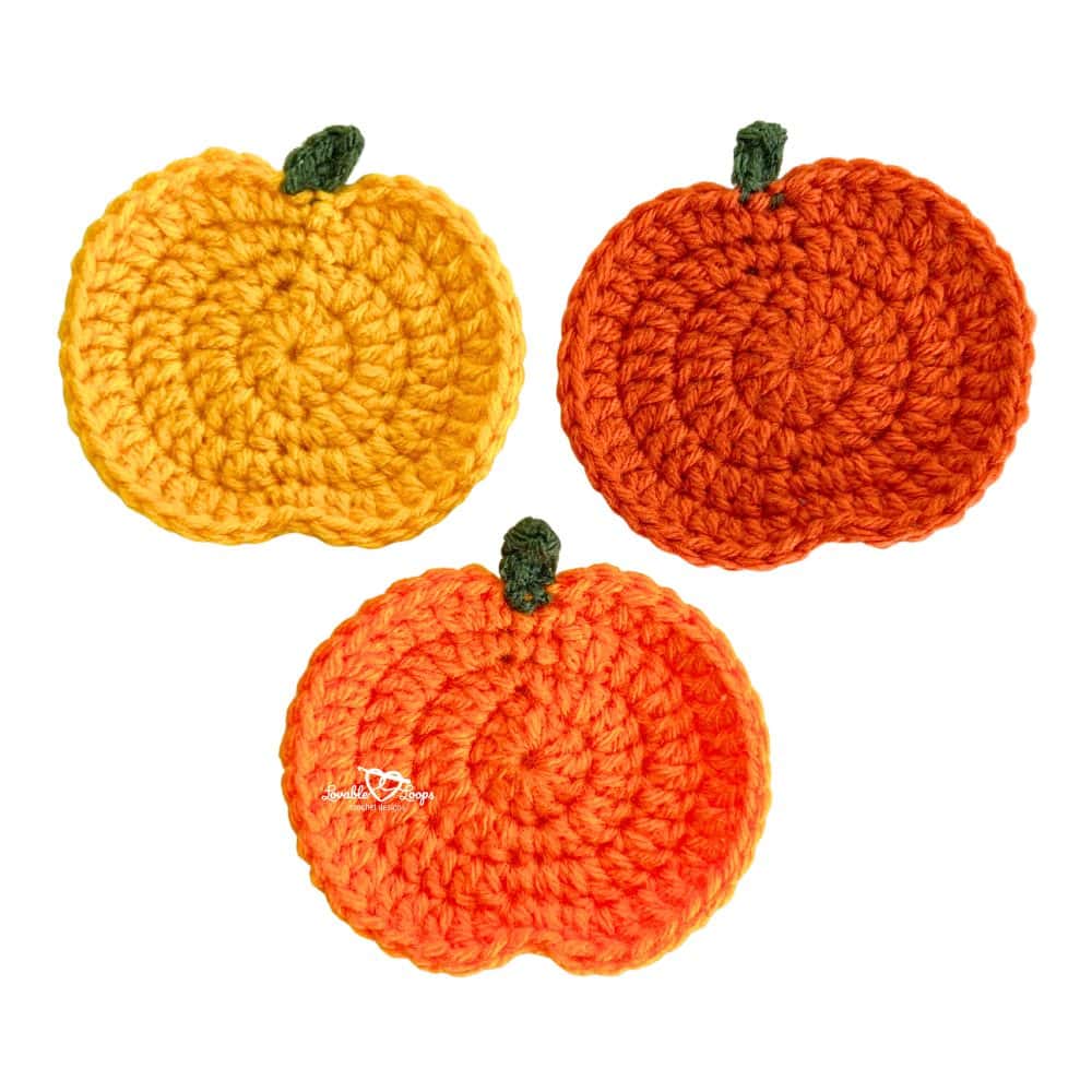 Three completed crochet pumpkin appliques in yellow, orange, and dark orange with green stems, made using a free and easy crochet pumpkin applique pattern.