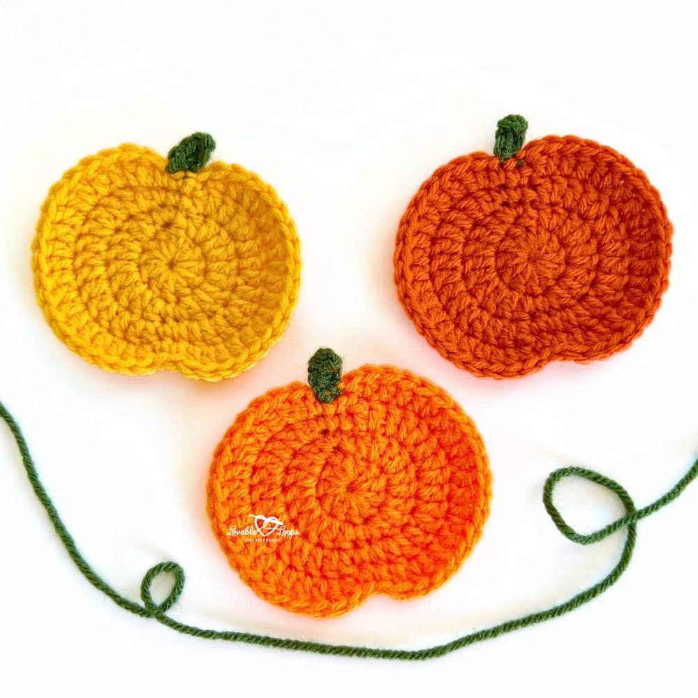 Three crochet pumpkin appliques in yellow, orange, and dark orange with green stems, displayed with a green yarn strand for an easy fall crochet project.