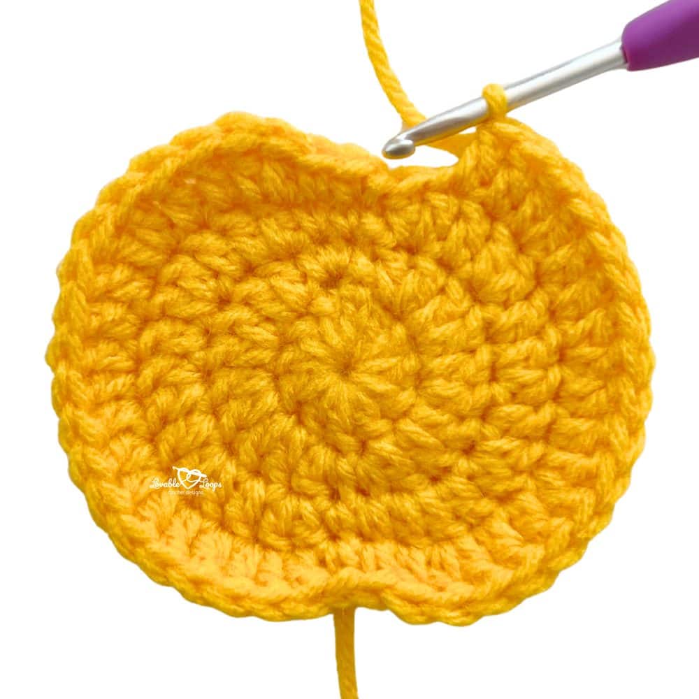 Close-up of a yellow crochet pumpkin applique in progress on the hook, showing how to make a free and beginner-friendly fall crochet applique pattern.