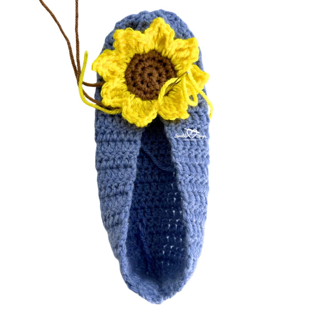 Blue crochet slipper with sunflower motif partly attached on the toe, showing work in progress from the free crochet sunflower slippers pattern.