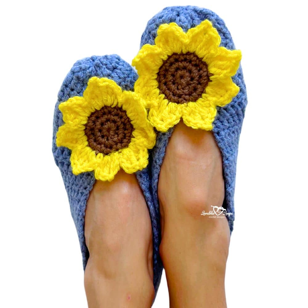 Finished pair of blue crochet slippers decorated with large yellow sunflower appliques, shown from above on feet.