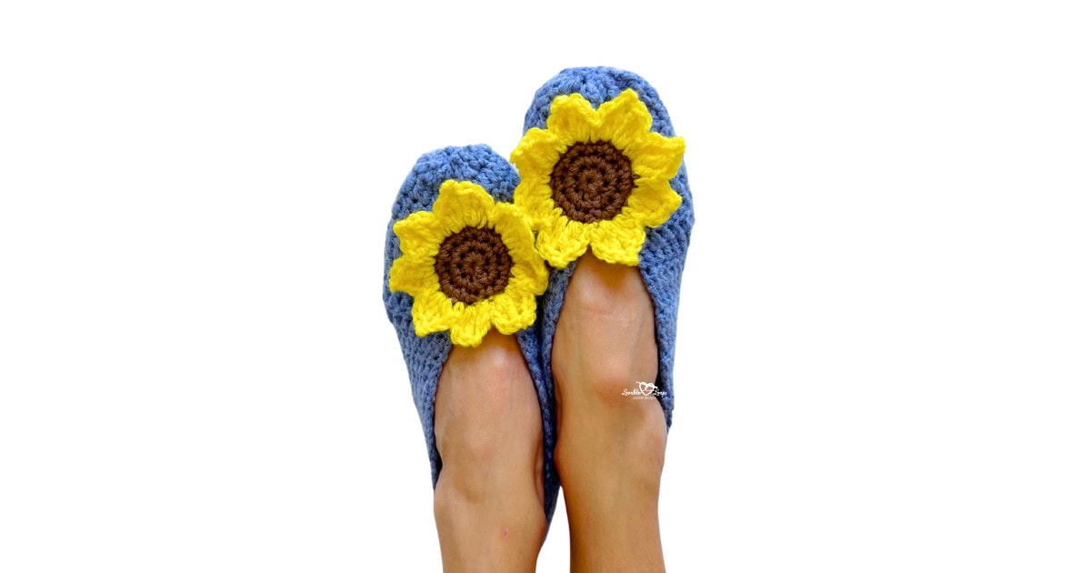 Handmade crochet house slippers decorated with bright yellow crochet sunflower motifs, shown in blue yarn. Free crochet slippers pattern for beginners.