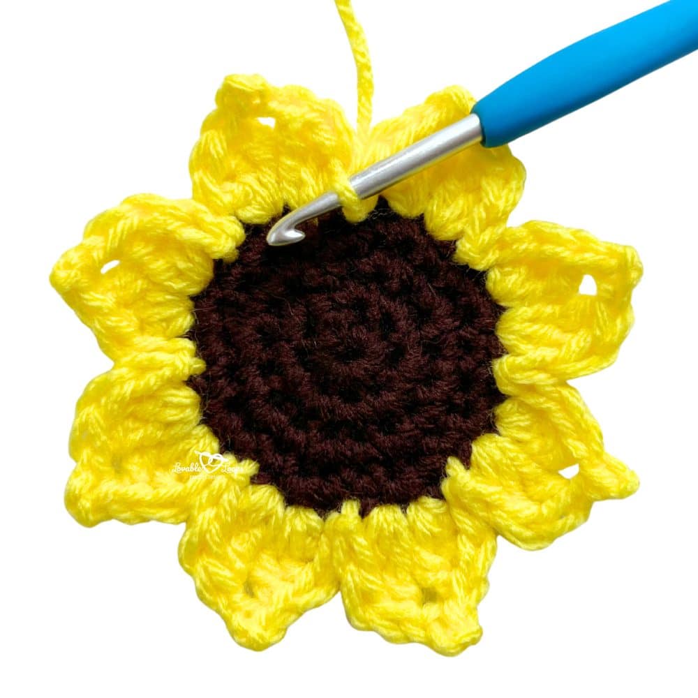 Close-up of a handmade sunflower crochet applique with yellow petals and a brown center. Quick and easy free crochet sunflower applique pattern for fall crafts and gifts.