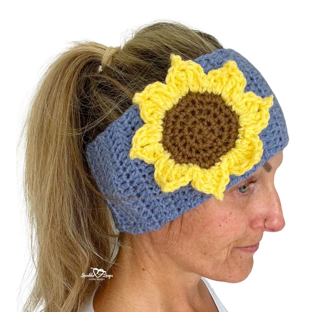 Woman wearing a crochet sunflower headband with a blue band and bright yellow flower applique on the side. Free crochet pattern tutorial.