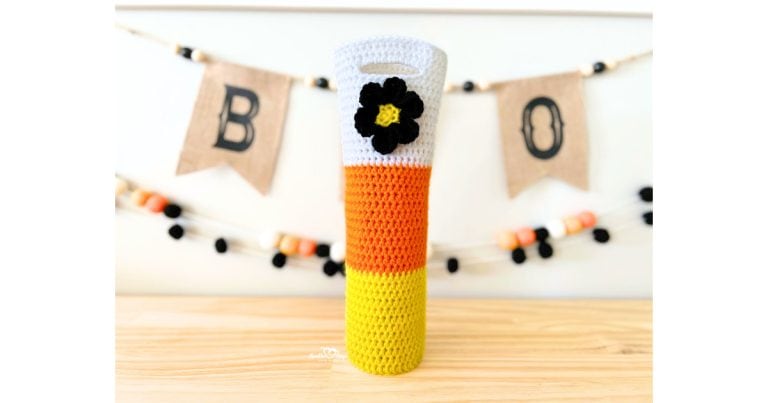 Festive crochet wine bottle bag in candy corn colors with a black flower, displayed with Halloween banner. Free crochet wine bottle holder pattern perfect for Halloween parties and fall gifting.