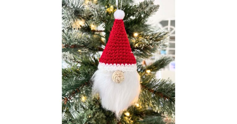 Handmade crochet gnome ornament with a red hat, faux fur beard, and pom pom hanging on a Christmas tree – free crochet Christmas gnome pattern.