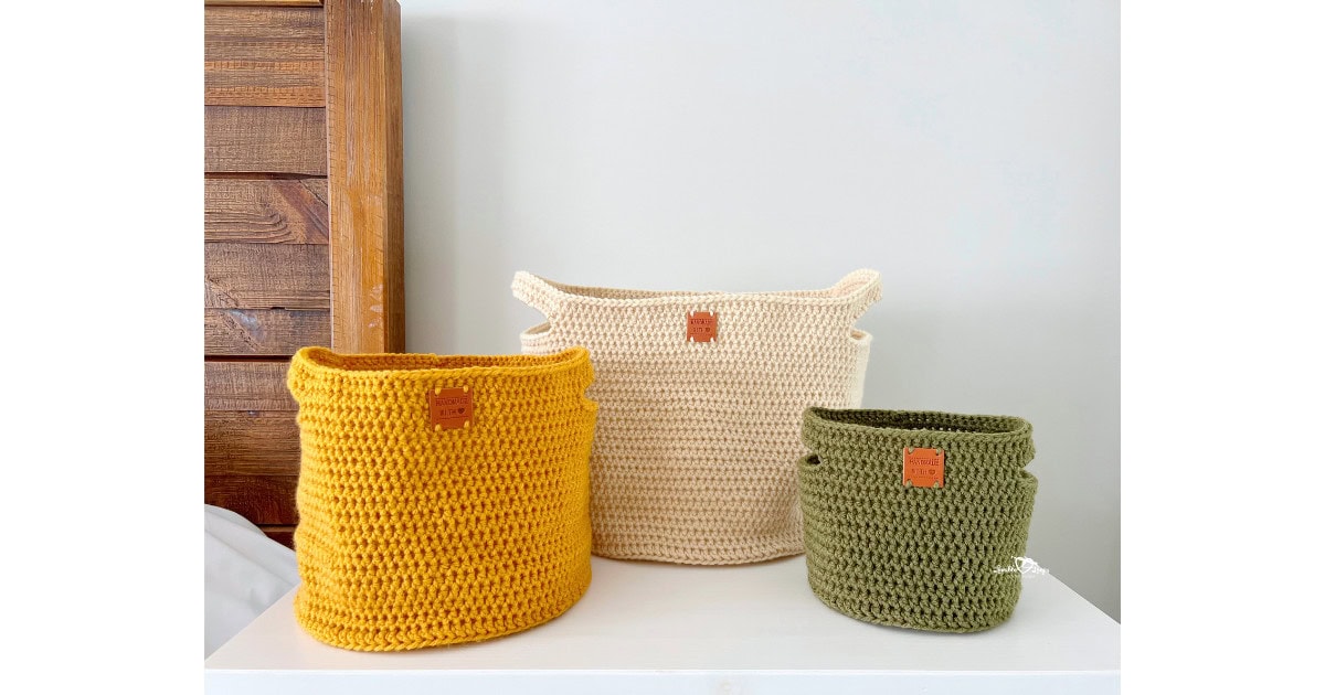 Three handmade crochet baskets in yellow, cream, and green yarn displayed on a shelf. Easy crochet basket pattern with handles available in three sizes.