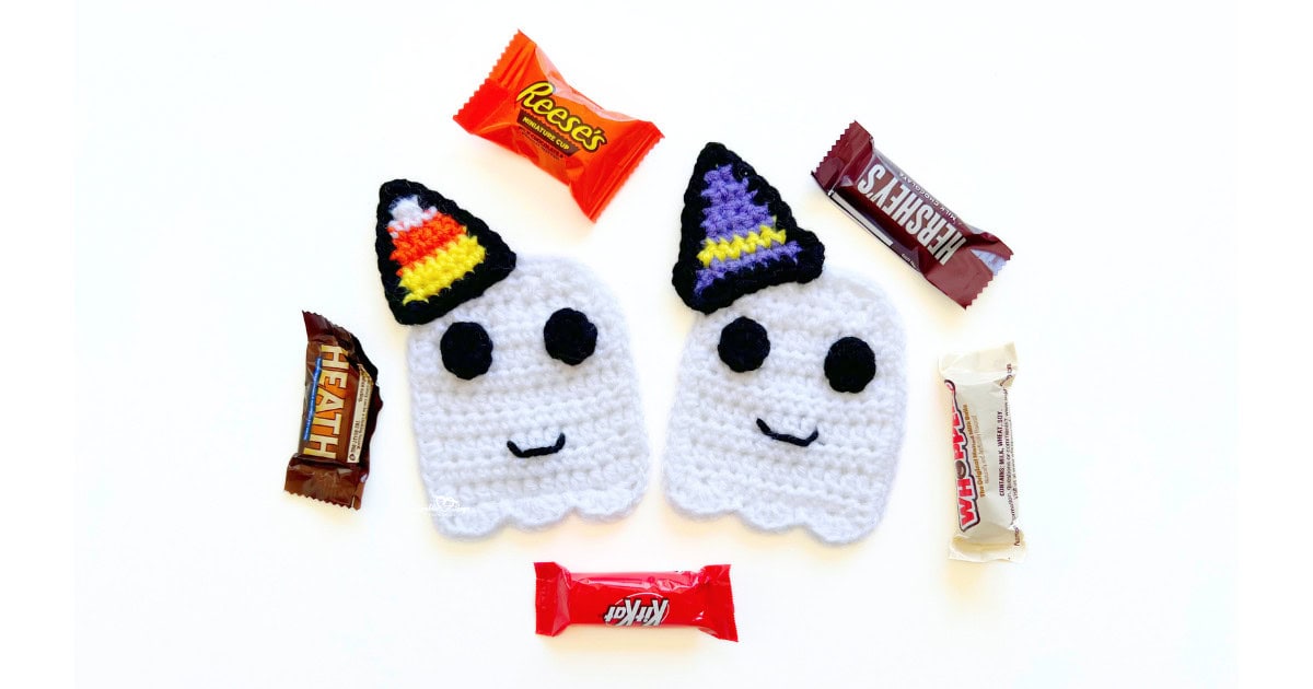 Two cute crochet ghost appliques with black eyes and smiles, each wearing a colorful Halloween hat, surrounded by candy bars. A fun free crochet ghost pattern for Halloween crafts and decorations.