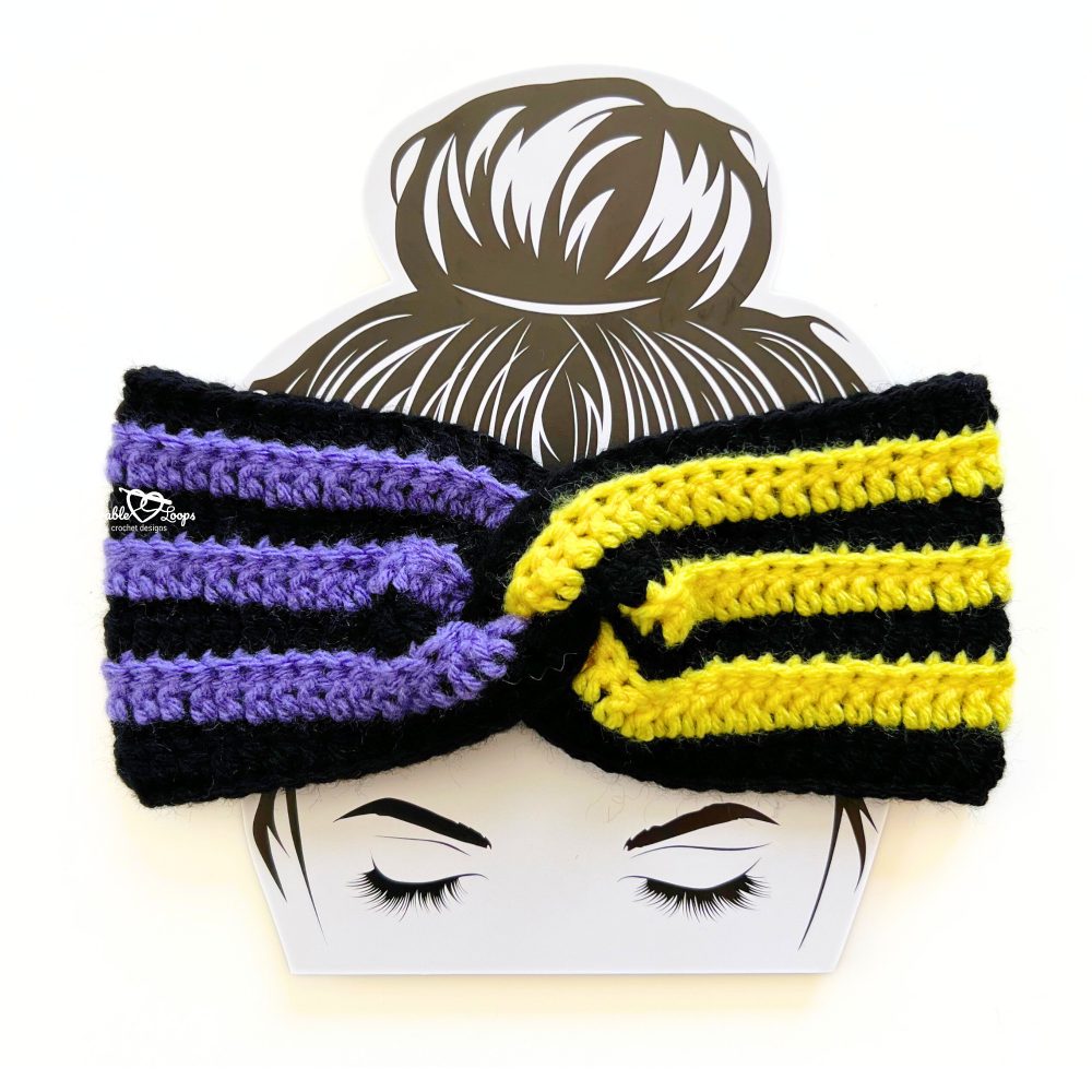Close-up of a crochet twisted headband in black, purple, and yellow stripes, featuring ribbed texture and twist front design.