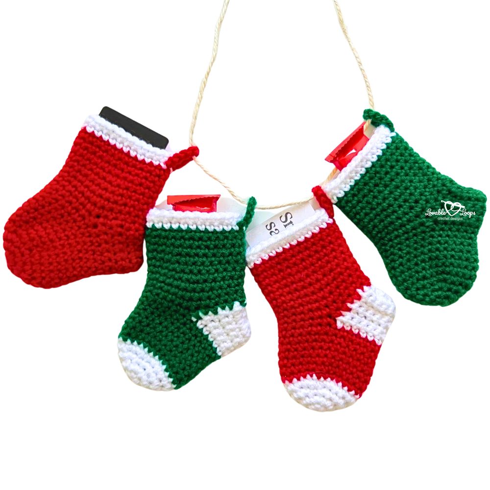 A garland of red and green crochet mini stockings strung on twine, each holding a treat. A fun and easy Christmas crochet idea for holiday décor.