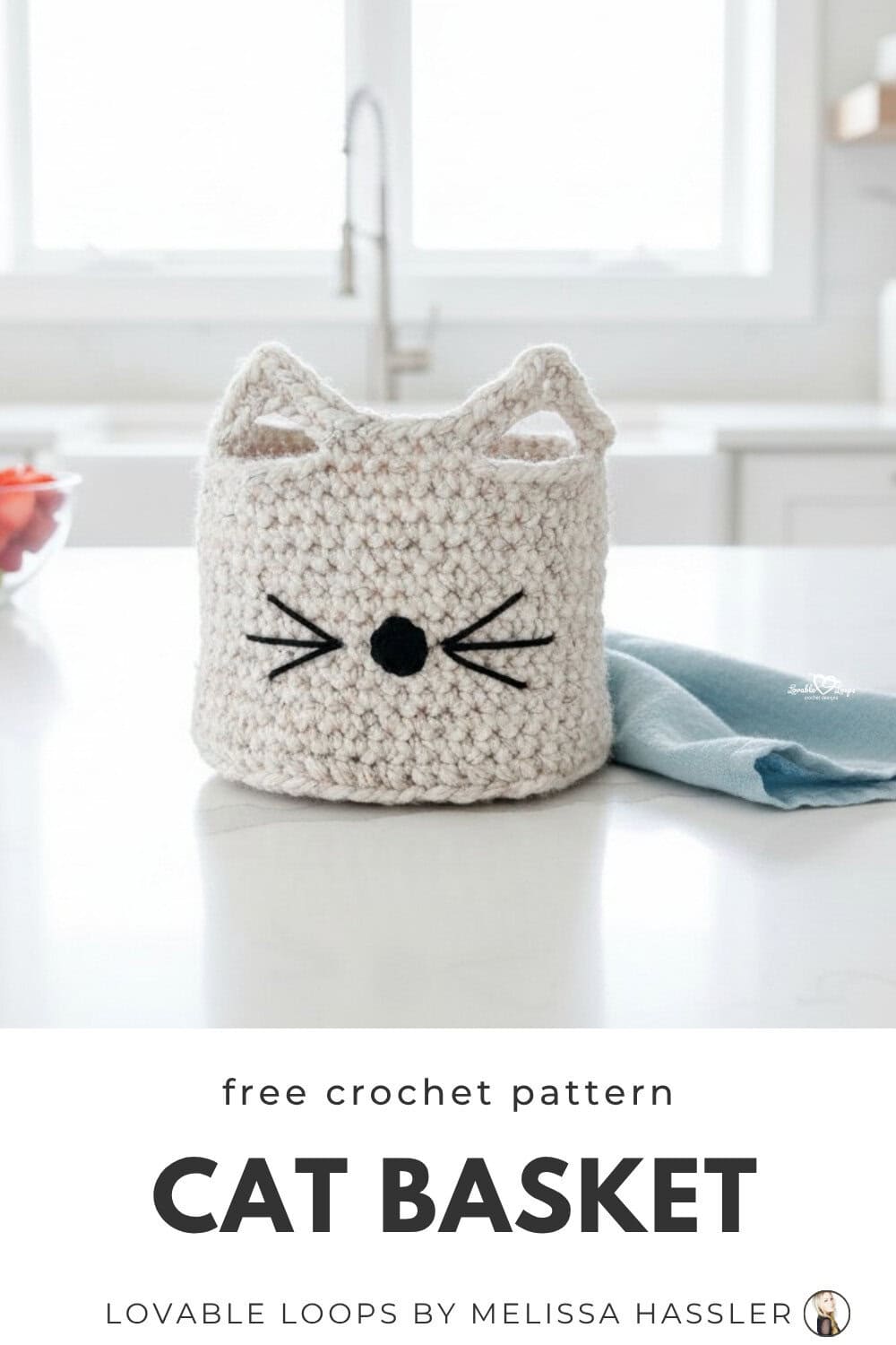 Handmade crochet cat basket with pointy ears and stitched whiskers sitting on a bright kitchen island with fresh colorful kitchen accents nearby.
