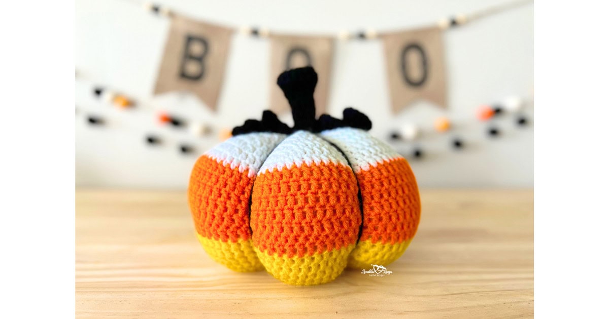 Handmade crochet pumpkin in candy corn colors of yellow, orange, and white with a black stem, styled as Halloween décor.