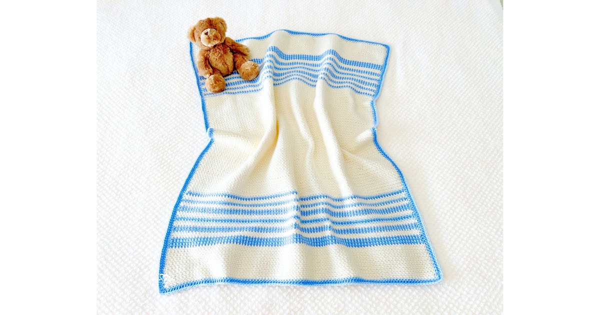 Cream and light blue moss stitch baby blanket crochet pattern with a teddy bear on top. A soft, beginner-friendly baby boy crochet blanket design.