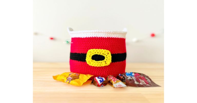 A handmade Santa basket crochet pattern in red with a black belt and yellow buckle, filled with holiday candy, perfect as a Christmas candy basket.