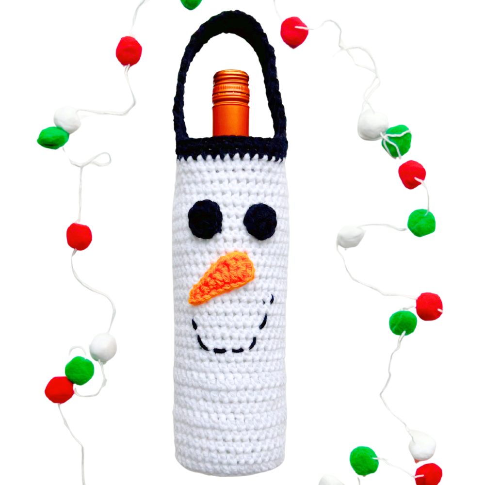 Crochet snowman wine bottle cover with black eyes, orange carrot nose, and stitched smile. A festive Christmas wine bottle holder crochet pattern for DIY holiday décor and gifting.