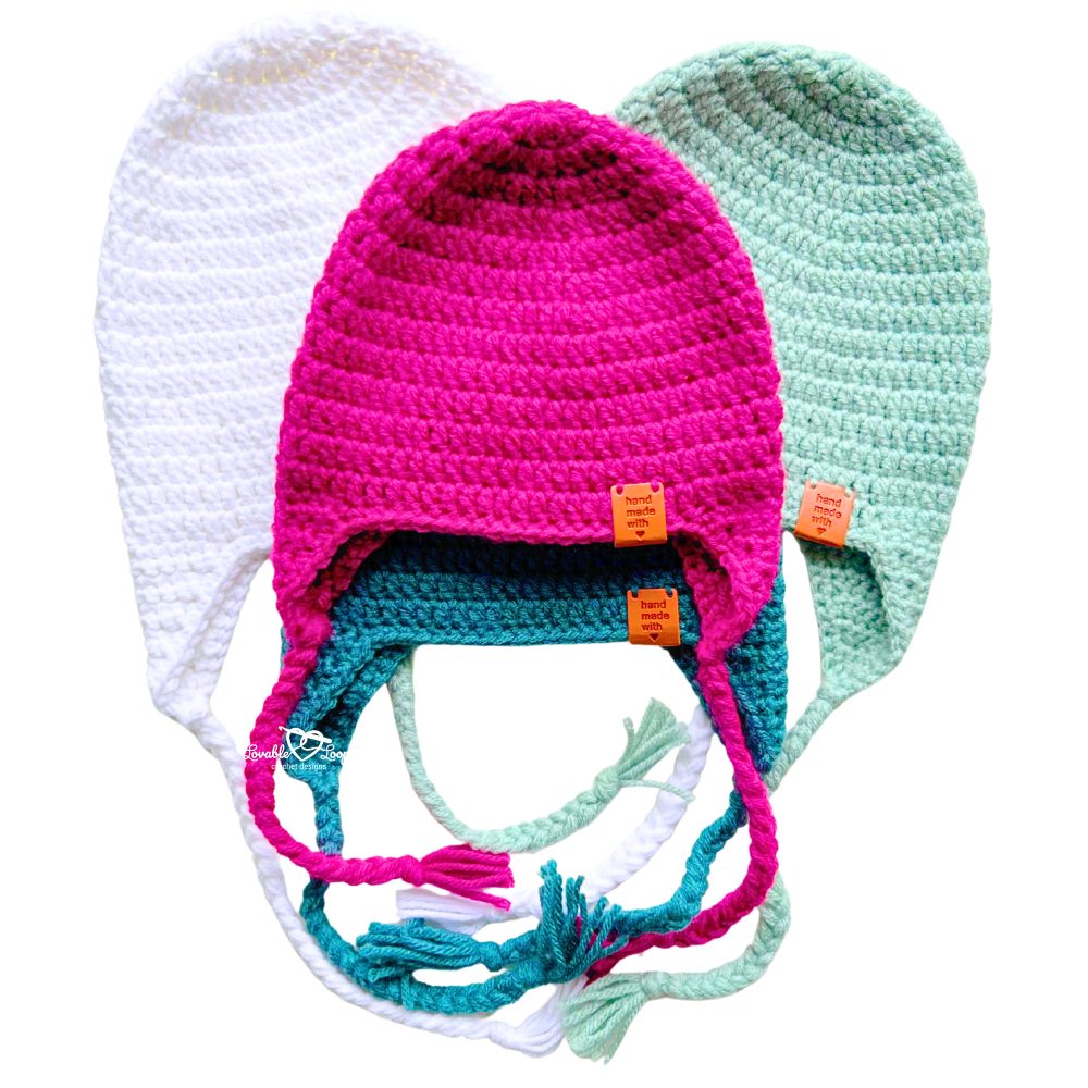 Three crochet earflap hats stacked together showing colorful braids and “handmade with love” tags. Easy crochet hat with ear flaps pattern for beginners by Lovable Loops.