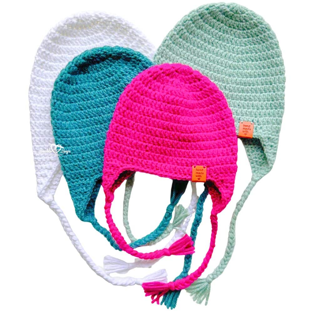 Four colorful crochet ear flap hats in white, teal, pink, and mint green displayed together. Beginner-friendly crochet hat with ear flaps pattern made with worsted weight yarn.