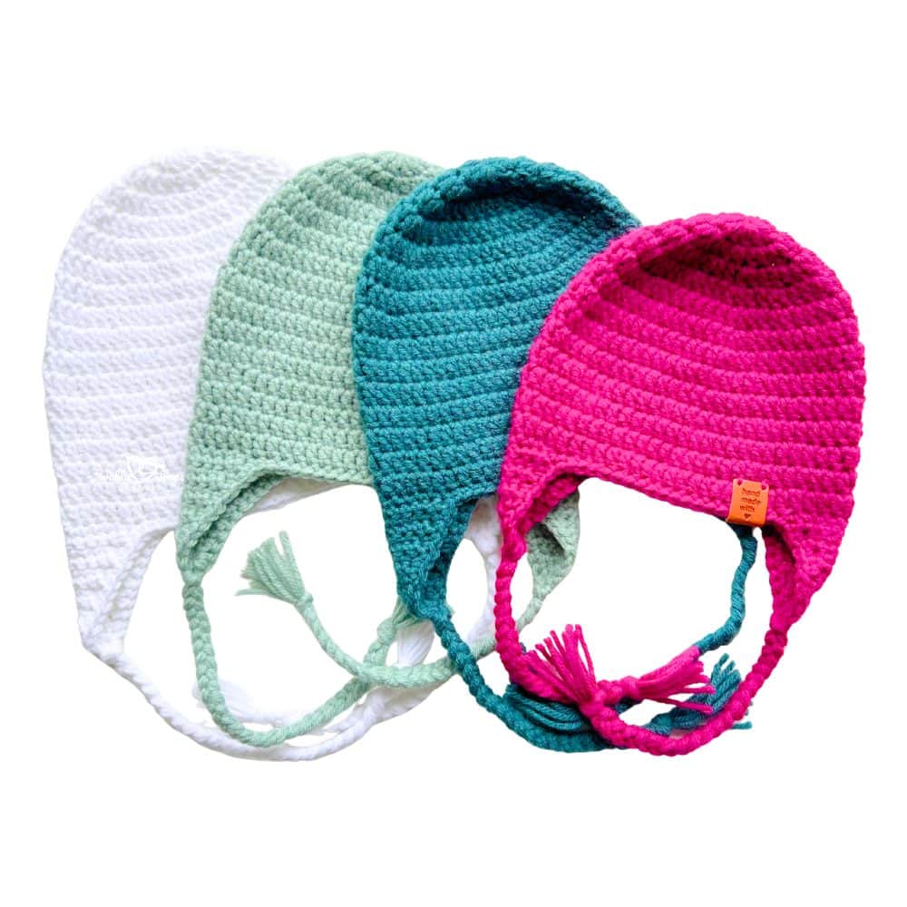 White, mint, teal, and bright pink crochet hats with ear flaps laid flat with braided ties. Free and easy crochet earflap hat pattern for baby, child, and adult sizes.