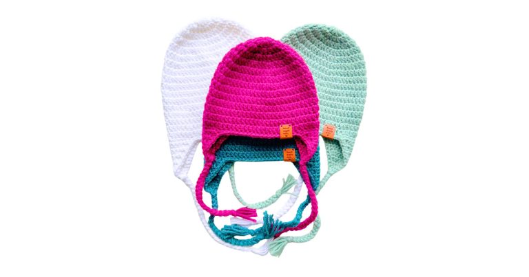 Three handmade crochet hats with ear flaps in white, pink, and mint green displayed flat on a white background. Beginner-friendly earflap hat crochet pattern made with worsted weight yarn.