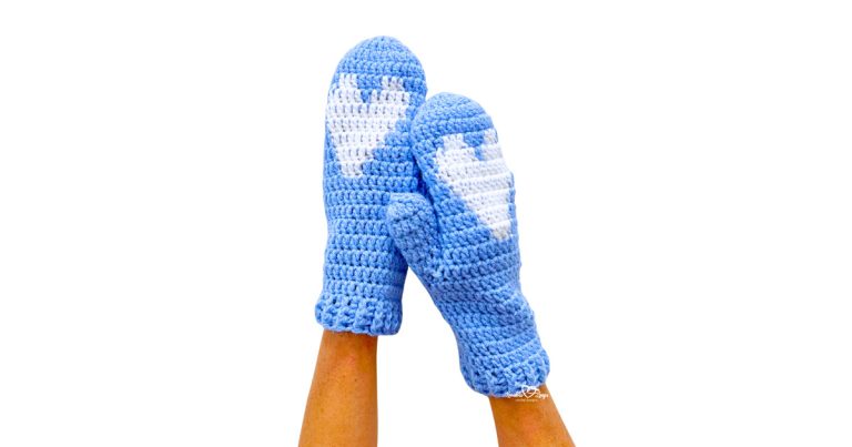 Two blue mittens with a white heart on each palm, ribbed cuffs, and neat stitches. Heart design crochet mittens in an easy crochet mittens colorwork pattern—cozy handmade mittens with heart motif for gifts.