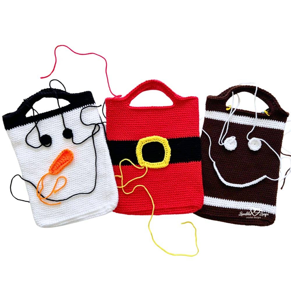 Three crochet Christmas bags in progress—a snowman, Santa, and gingerbread man—each with yarn tails and embellishments being attached.