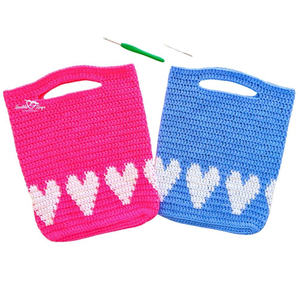 Square photo of two rectangular crochet bags—one pink, one blue—each with rows of white hearts and a built-in handle; heart crochet bag pattern for advanced beginners.