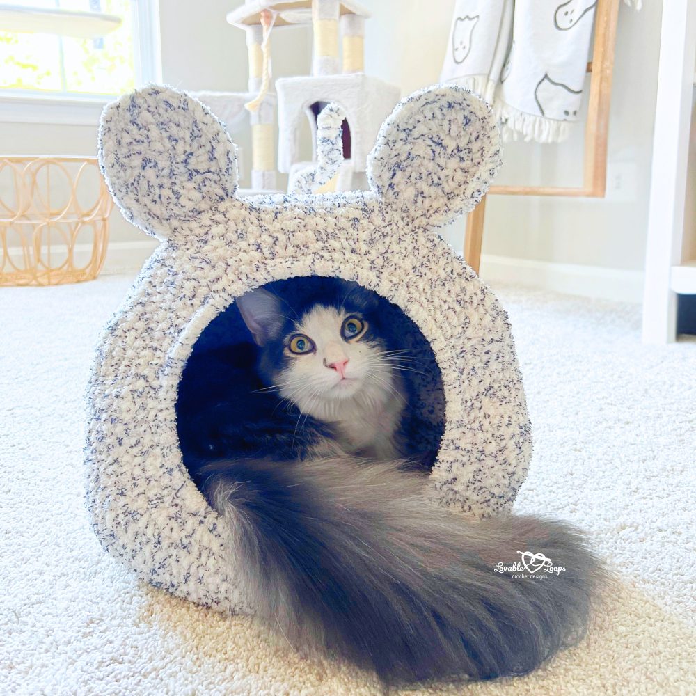 Gray and white cat resting inside a soft crochet cat cave with mouse ears and tail, made from chunky blanket yarn. DIY crochet cat pod pattern for beginners.