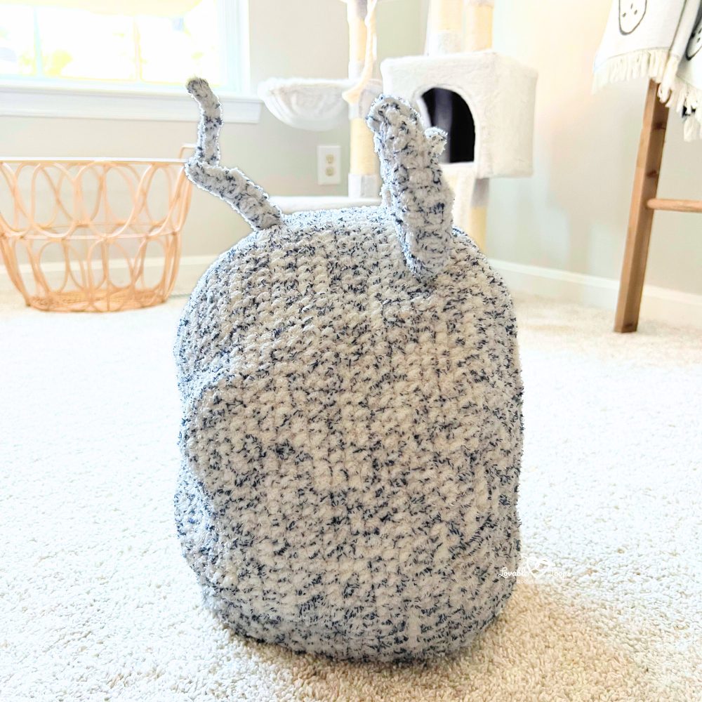 Close-up of the mouse-shaped crochet cat cave showing round ears and a curly tail made from soft gray and white blanket yarn.