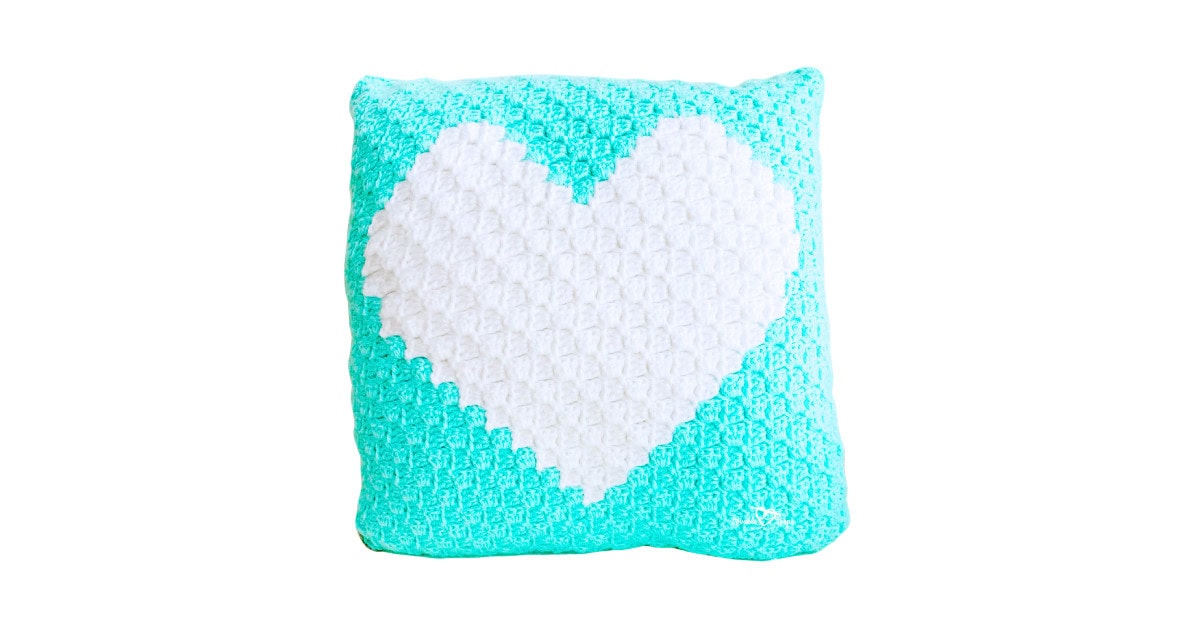 Crochet heart pillow made with the corner-to-corner (C2C) method, featuring a white heart design on a teal background, perfect for beginner-friendly crochet home d&eacute;cor.