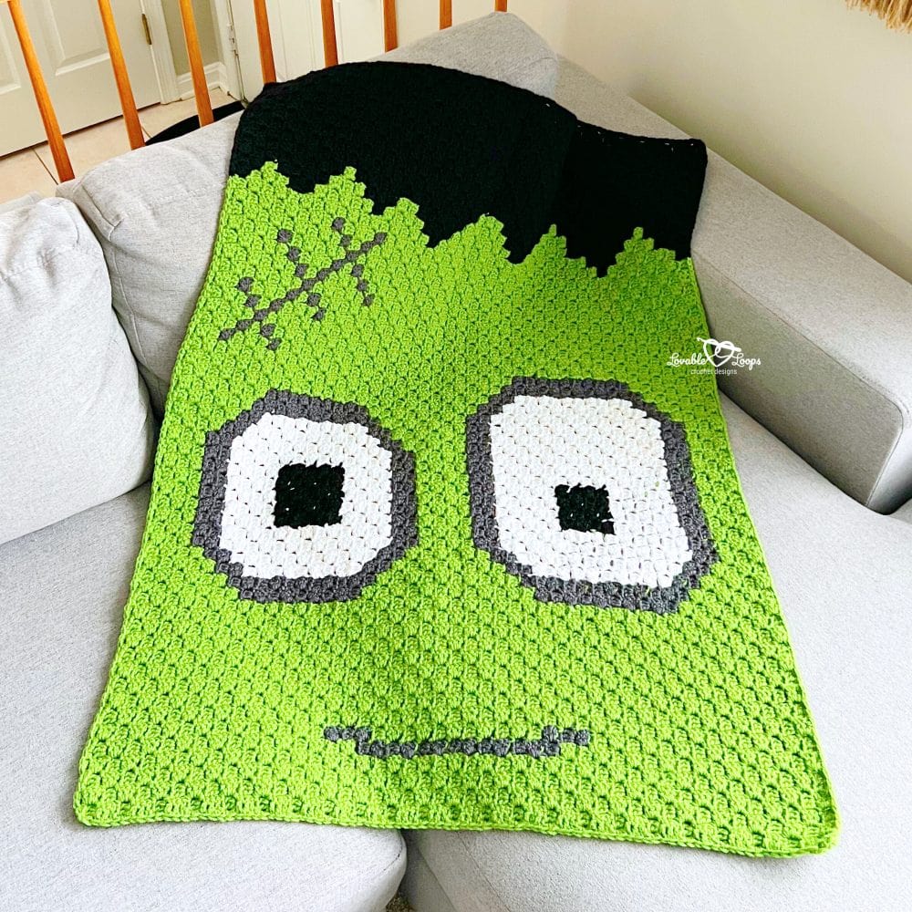 Close-up of a Frankenstein face on a C2C crochet blanket, showing detailed corner-to-corner colorwork in green, black, white, and gray yarn.
