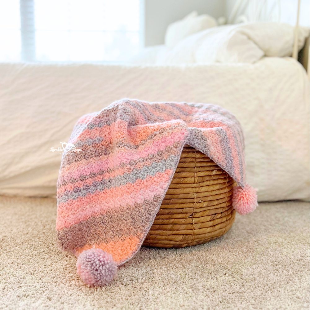 Easy C2C baby blanket crochet pattern folded over a woven basket, showing the diagonal corner-to-corner stitch texture