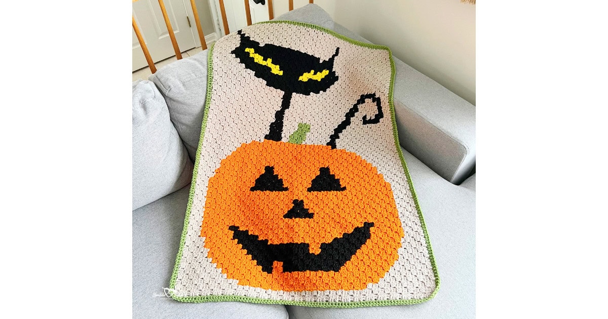 C2C jack o lantern pumpkin blanket crochet pattern with a smiling pumpkin face and bold Halloween colorwork, shown on a couch