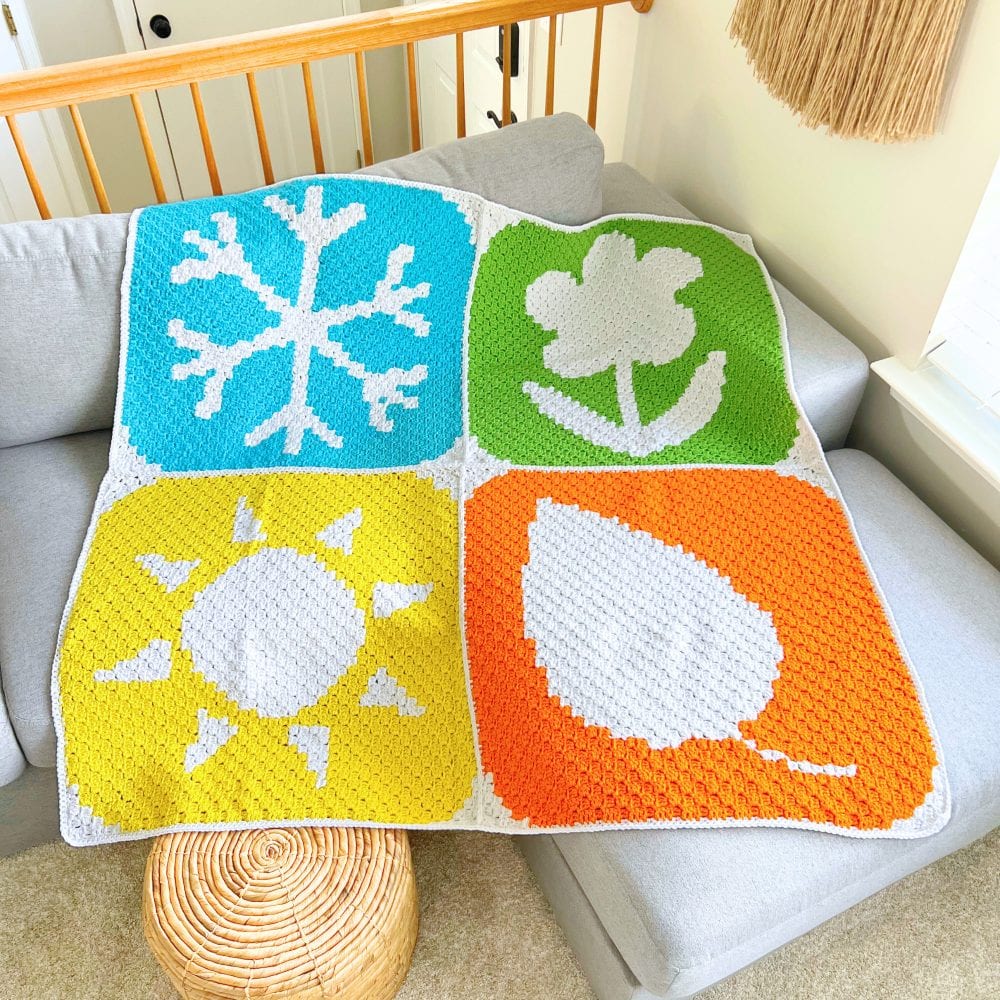 Finished C2C seasons blanket crochet pattern showing four seasonal panels joined together with a border, displayed on a couch