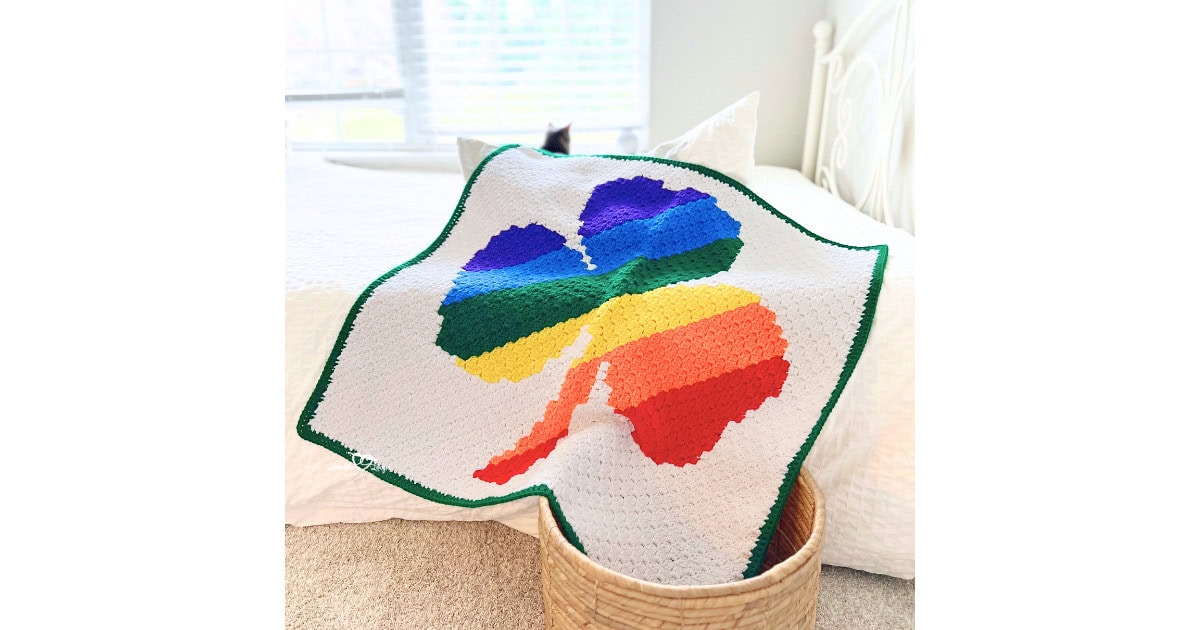 Corner-to-corner shamrock crochet blanket with a green border, shown draped on a bed for St. Patrick’s Day
